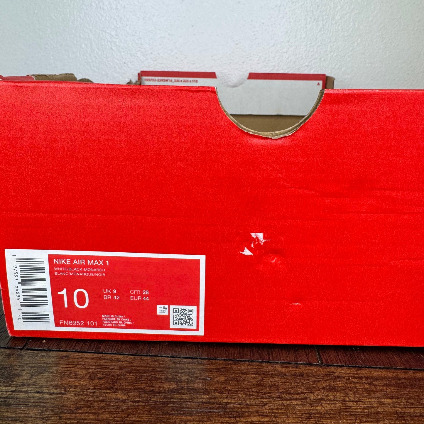 Red Nike Air Max box with size 10 label on a wooden surface.